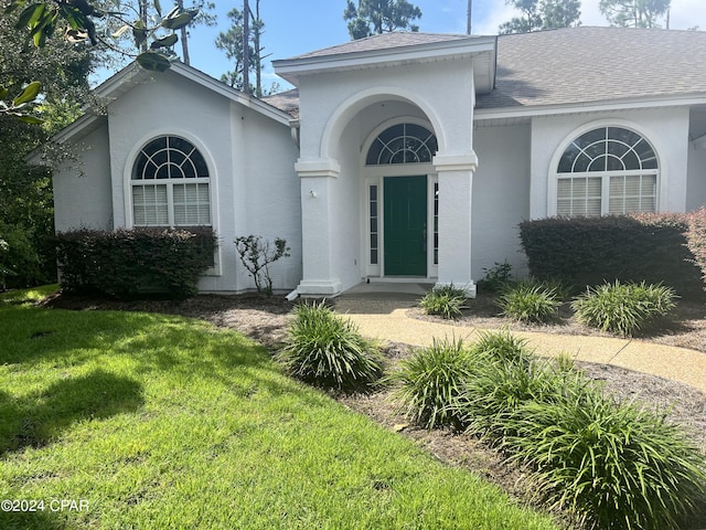 view of front of home with stucco siding, roof with shingles, and a front yard