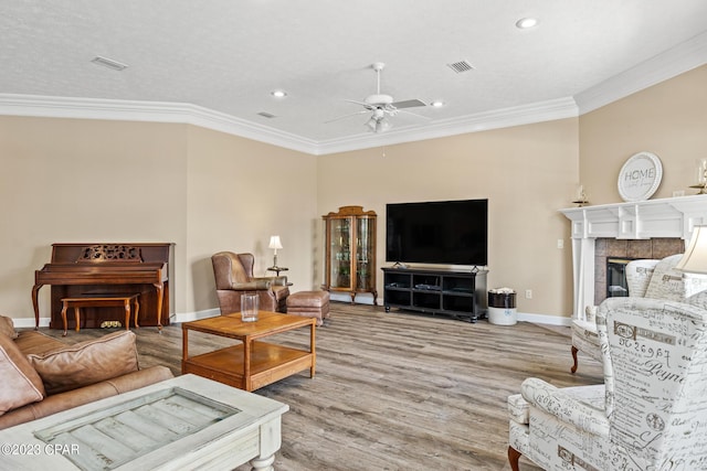 living area featuring a tiled fireplace, wood finished floors, visible vents, and ornamental molding