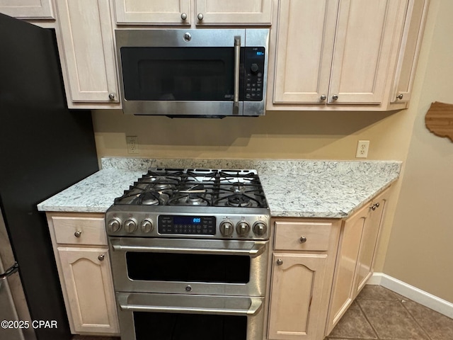 kitchen with tile patterned flooring, light stone counters, appliances with stainless steel finishes, and baseboards