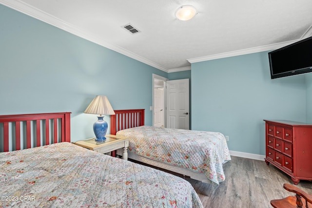 bedroom featuring visible vents, baseboards, wood finished floors, and crown molding