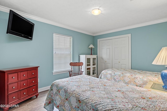 bedroom with a closet, ornamental molding, baseboards, and wood finished floors