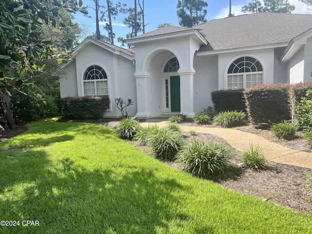 view of front of house with stucco siding, a shingled roof, and a front yard