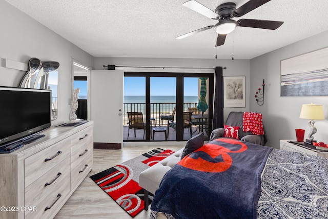 bedroom featuring light hardwood / wood-style floors, a water view, access to exterior, a textured ceiling, and ceiling fan