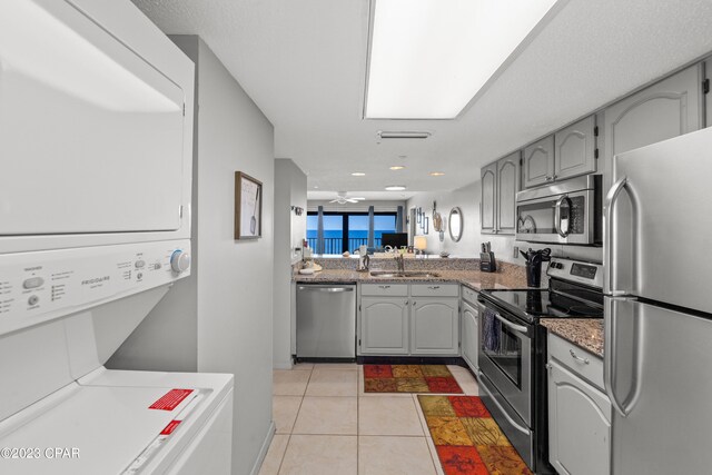 kitchen with appliances with stainless steel finishes, stacked washer / drying machine, sink, and gray cabinets