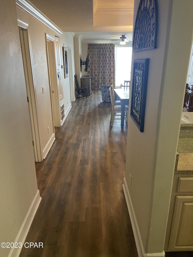 corridor with a textured ceiling, ornamental molding, and dark wood-type flooring