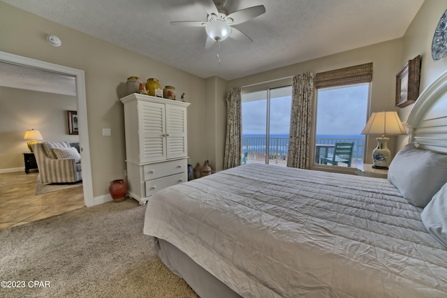 bedroom with access to outside, a water view, ceiling fan, a textured ceiling, and light colored carpet