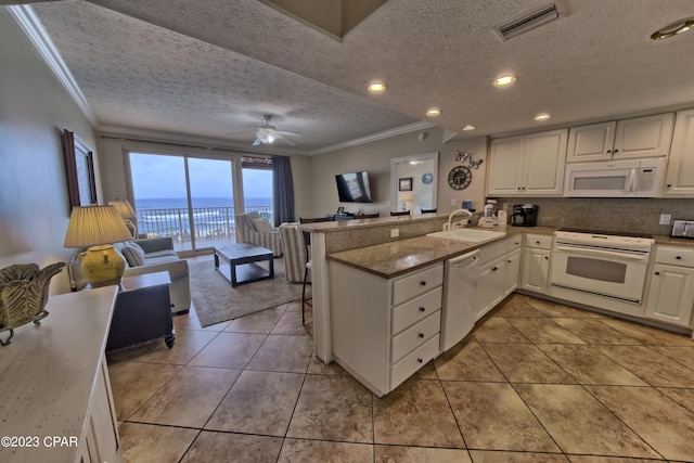 kitchen with kitchen peninsula, a textured ceiling, white appliances, sink, and white cabinetry