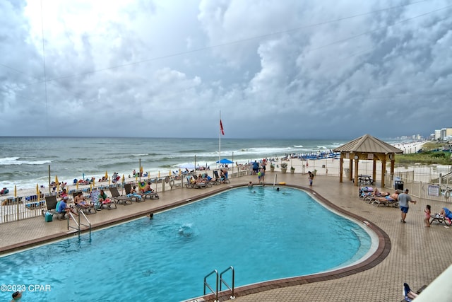 view of pool featuring a water view, a patio, and a beach view