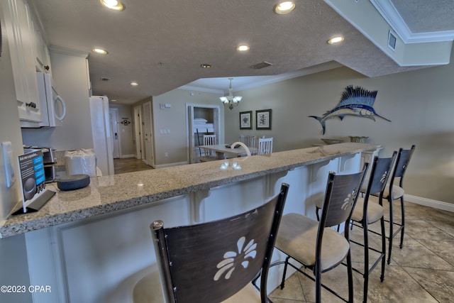 kitchen with pendant lighting, a breakfast bar, ornamental molding, a notable chandelier, and white cabinetry