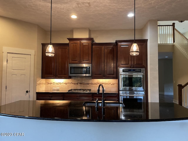 kitchen with pendant lighting, tasteful backsplash, appliances with stainless steel finishes, dark stone countertops, and sink