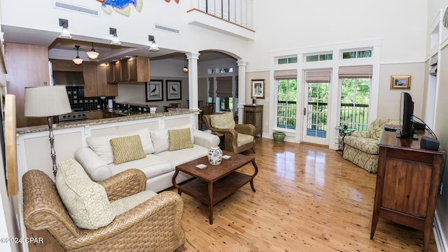 living room featuring sink, a high ceiling, decorative columns, and light hardwood / wood-style floors