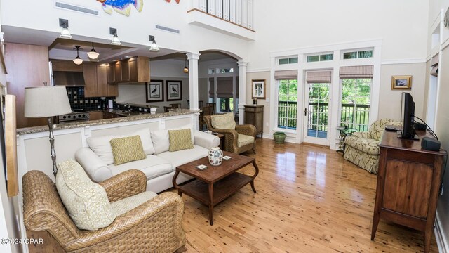 living room with light wood-style flooring, visible vents, ornate columns, and a high ceiling