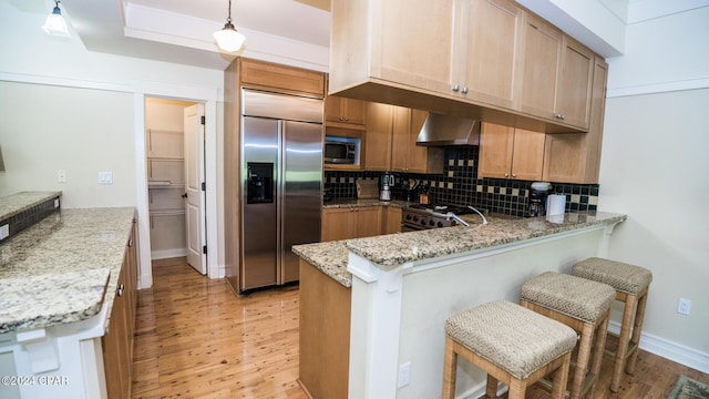 kitchen featuring built in appliances, wall chimney range hood, a peninsula, and light wood-style flooring