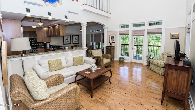 living room with light wood-style flooring, visible vents, ornate columns, and a high ceiling