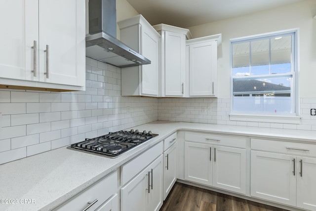 kitchen with wall chimney exhaust hood, tasteful backsplash, light stone counters, white cabinetry, and stainless steel gas cooktop