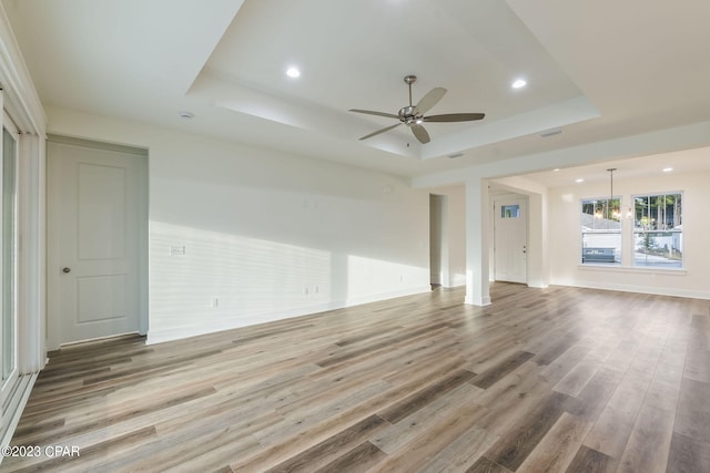 unfurnished living room featuring hardwood / wood-style floors, ceiling fan with notable chandelier, and a tray ceiling