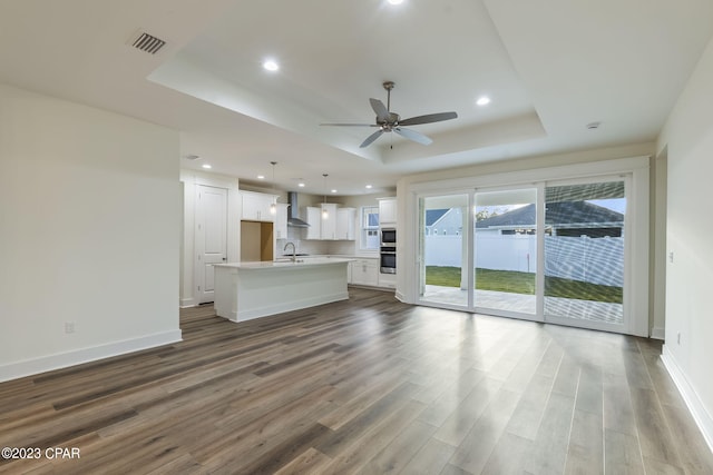 unfurnished living room with a tray ceiling, ceiling fan, sink, and dark wood-type flooring