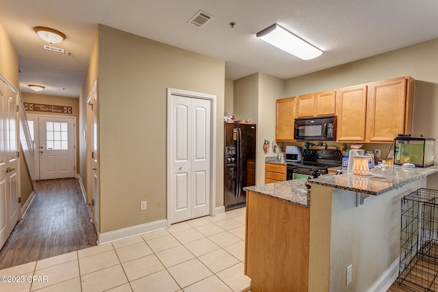 kitchen with kitchen peninsula, black appliances, light tile flooring, a kitchen breakfast bar, and dark stone countertops