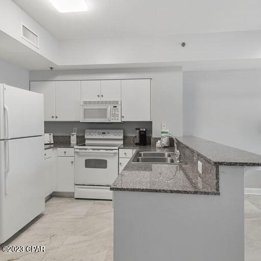 kitchen with kitchen peninsula, white appliances, sink, light tile flooring, and white cabinetry