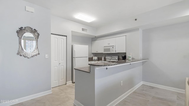 kitchen with light tile flooring, kitchen peninsula, white appliances, white cabinets, and dark stone countertops