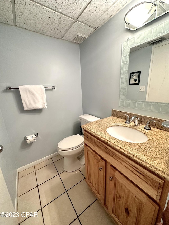 bathroom with toilet, vanity with extensive cabinet space, tile floors, and a drop ceiling