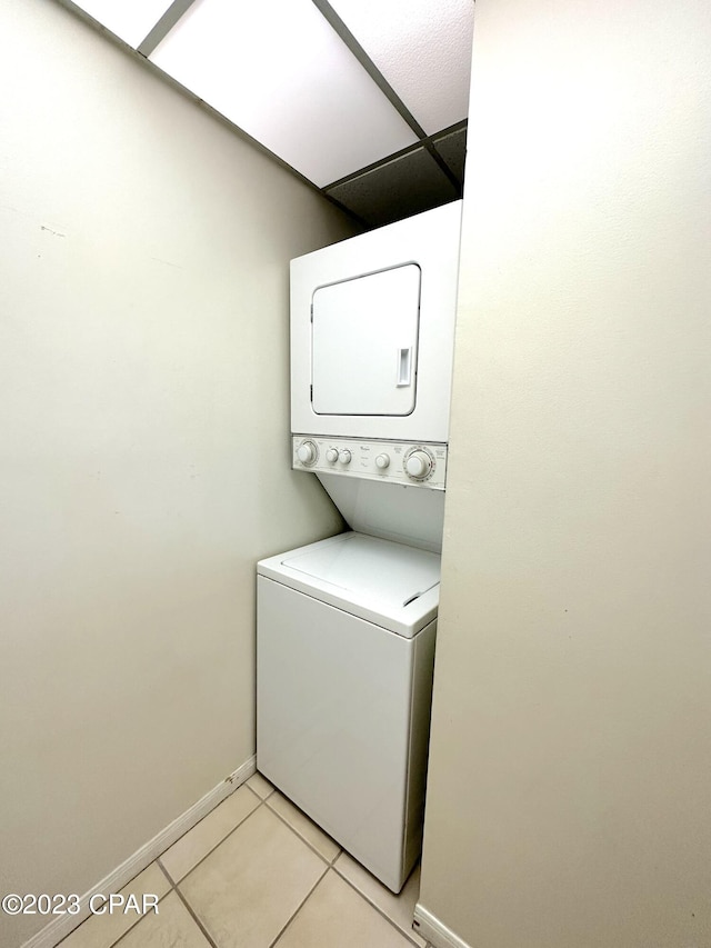 laundry room featuring stacked washer / drying machine and light tile flooring