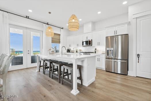 kitchen featuring a breakfast bar, decorative light fixtures, white cabinetry, stainless steel appliances, and a center island with sink