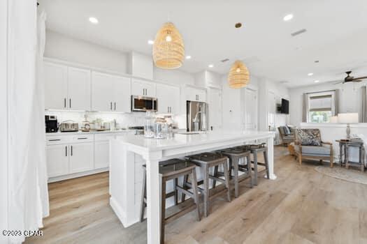 kitchen featuring stainless steel appliances, an island with sink, a breakfast bar area, and white cabinetry