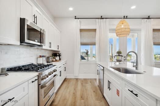 kitchen with sink, hanging light fixtures, stainless steel appliances, white cabinets, and decorative backsplash