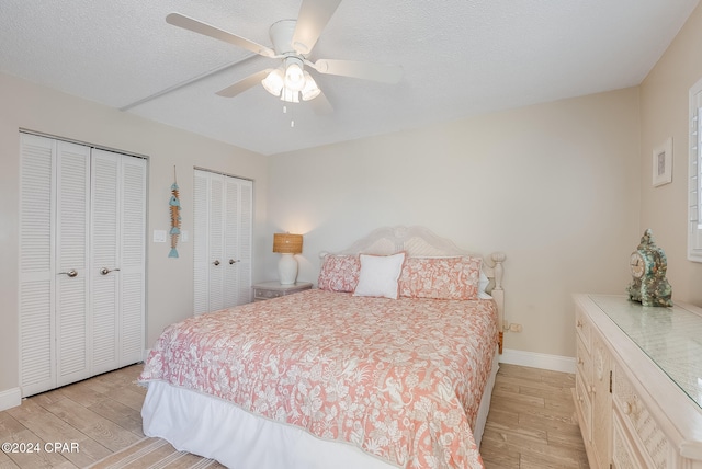 bedroom featuring ceiling fan, multiple closets, a textured ceiling, and light hardwood / wood-style flooring