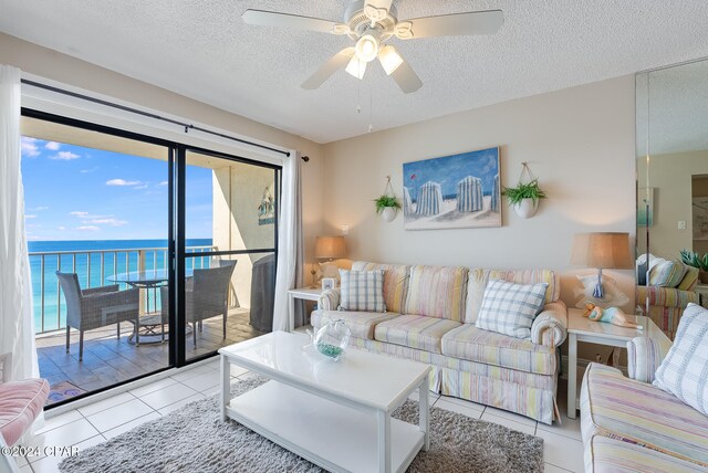 living room featuring ceiling fan, light tile patterned flooring, a water view, and a textured ceiling