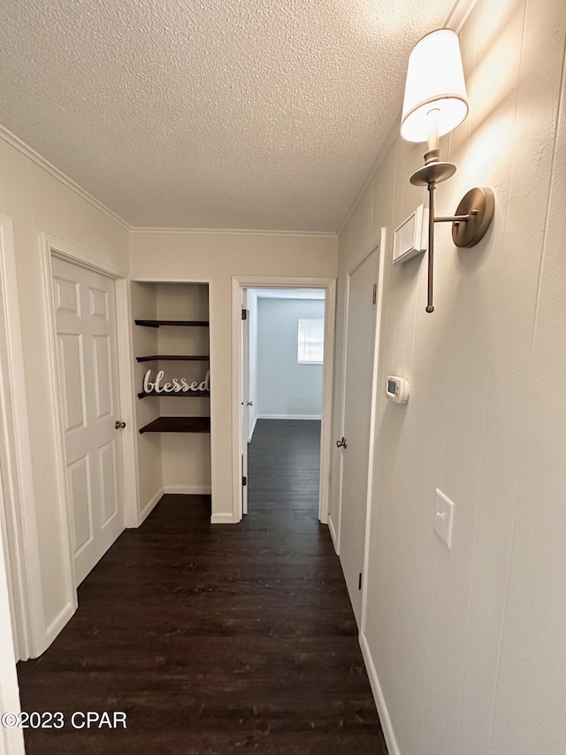 hallway with crown molding, built in features, dark hardwood / wood-style floors, and a textured ceiling