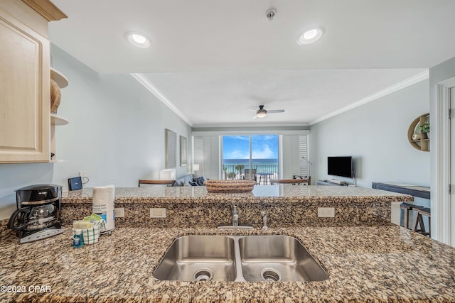 kitchen with crown molding, light brown cabinetry, ceiling fan, dark stone counters, and sink