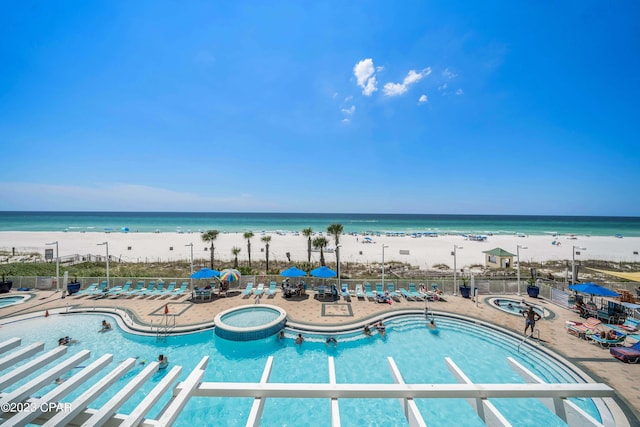 view of pool featuring a patio, a water view, and a beach view