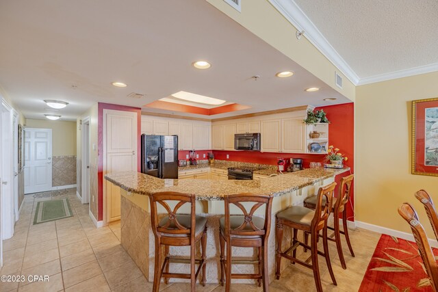 kitchen featuring a breakfast bar, light tile patterned flooring, black appliances, ornamental molding, and light stone countertops