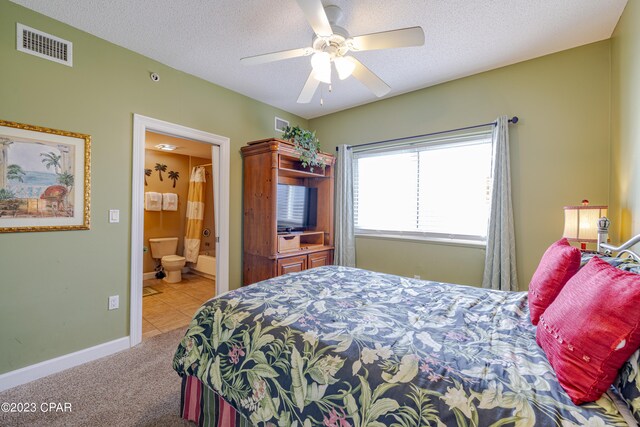 bedroom featuring ceiling fan, a textured ceiling, light carpet, and ensuite bathroom