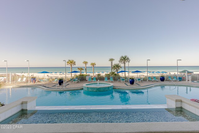 view of swimming pool featuring a hot tub, a water view, and a patio area