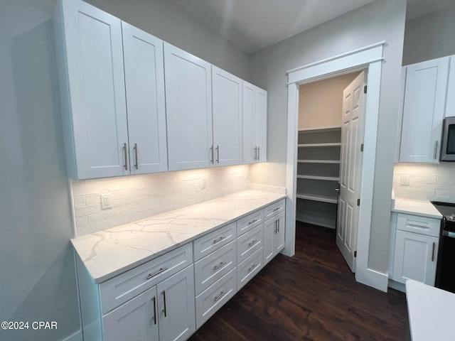 kitchen with white cabinets, backsplash, light stone countertops, and dark hardwood / wood-style floors