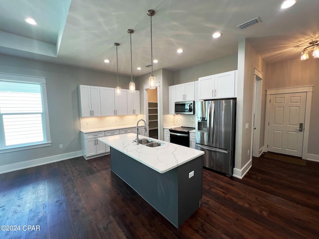 kitchen with dark wood-type flooring, sink, stainless steel appliances, a center island with sink, and light stone countertops