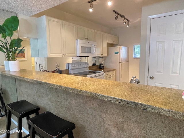 kitchen with rail lighting, white cabinetry, a breakfast bar, white appliances, and a textured ceiling