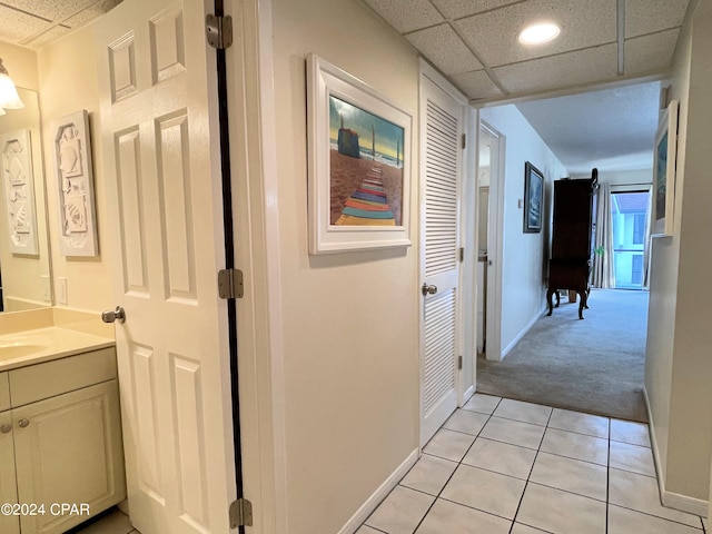 hallway featuring sink, a drop ceiling, and light tile patterned floors