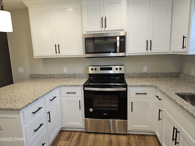 kitchen with stainless steel appliances, white cabinetry, light stone countertops, and wood-type flooring