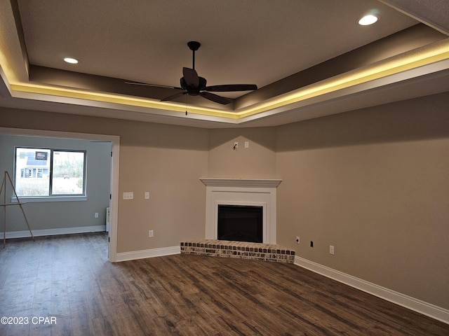 unfurnished living room featuring a raised ceiling, dark hardwood / wood-style floors, a fireplace, and ceiling fan