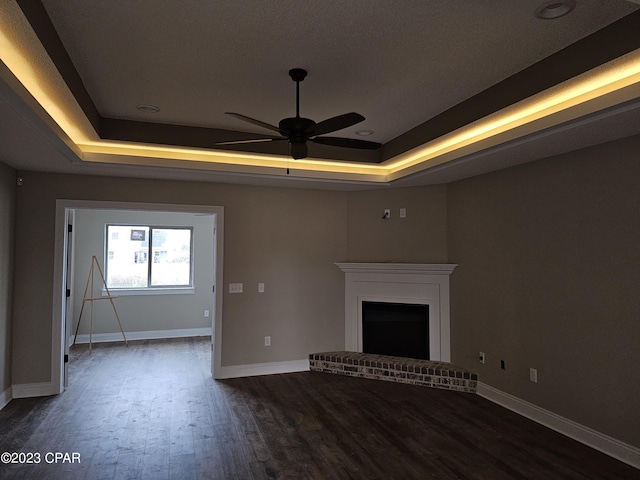 unfurnished living room featuring dark hardwood / wood-style floors, a fireplace, ceiling fan, and a tray ceiling