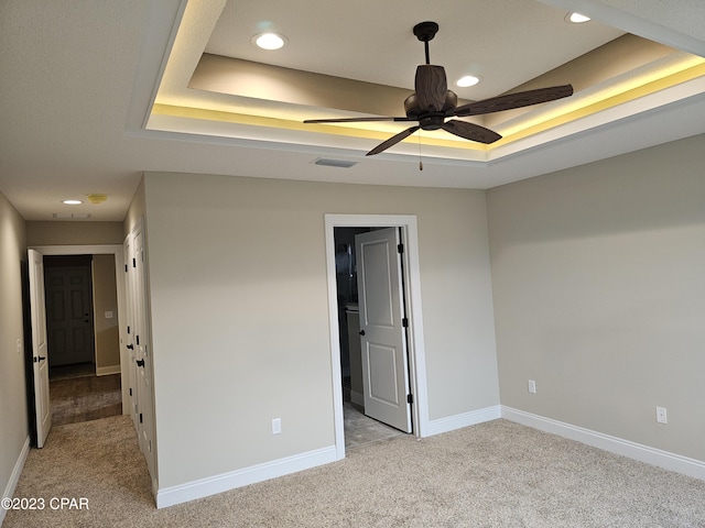 carpeted spare room featuring ceiling fan and a raised ceiling