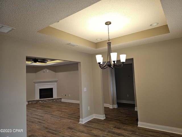 interior space with a brick fireplace, ceiling fan with notable chandelier, dark hardwood / wood-style flooring, and a tray ceiling