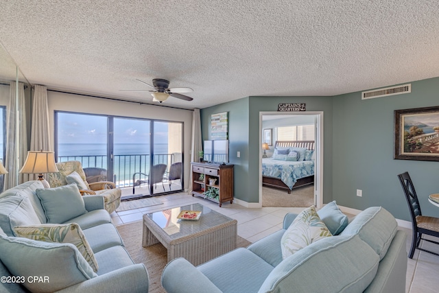 tiled living room featuring a textured ceiling, ceiling fan, and a water view