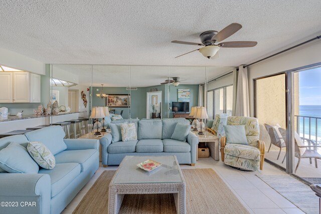 tiled living room featuring a water view, a textured ceiling, and ceiling fan with notable chandelier