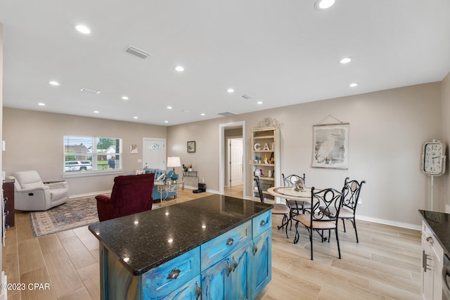 kitchen with dark stone countertops, a center island, light hardwood / wood-style floors, and blue cabinetry