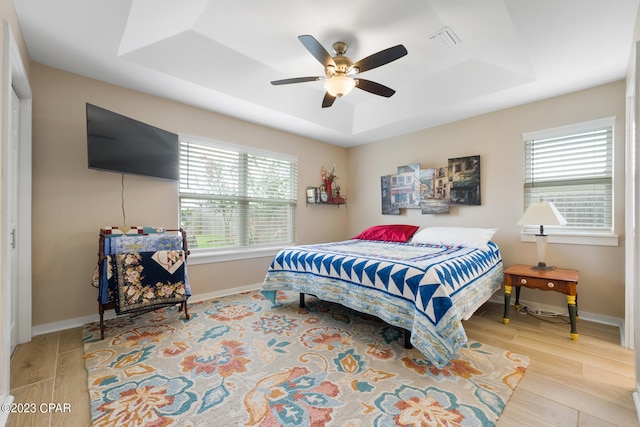 bedroom featuring a raised ceiling, a closet, ceiling fan, and light hardwood / wood-style floors